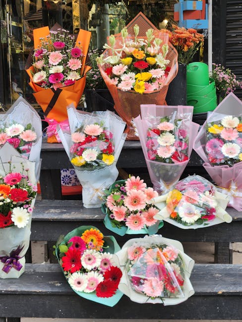 A display of various bouquets of fresh flowers arranged on wooden steps outside a shop, featuring a mix of pink, white, yellow, red, and purple blooms including daisies, Gerbera daisies, roses, and ch